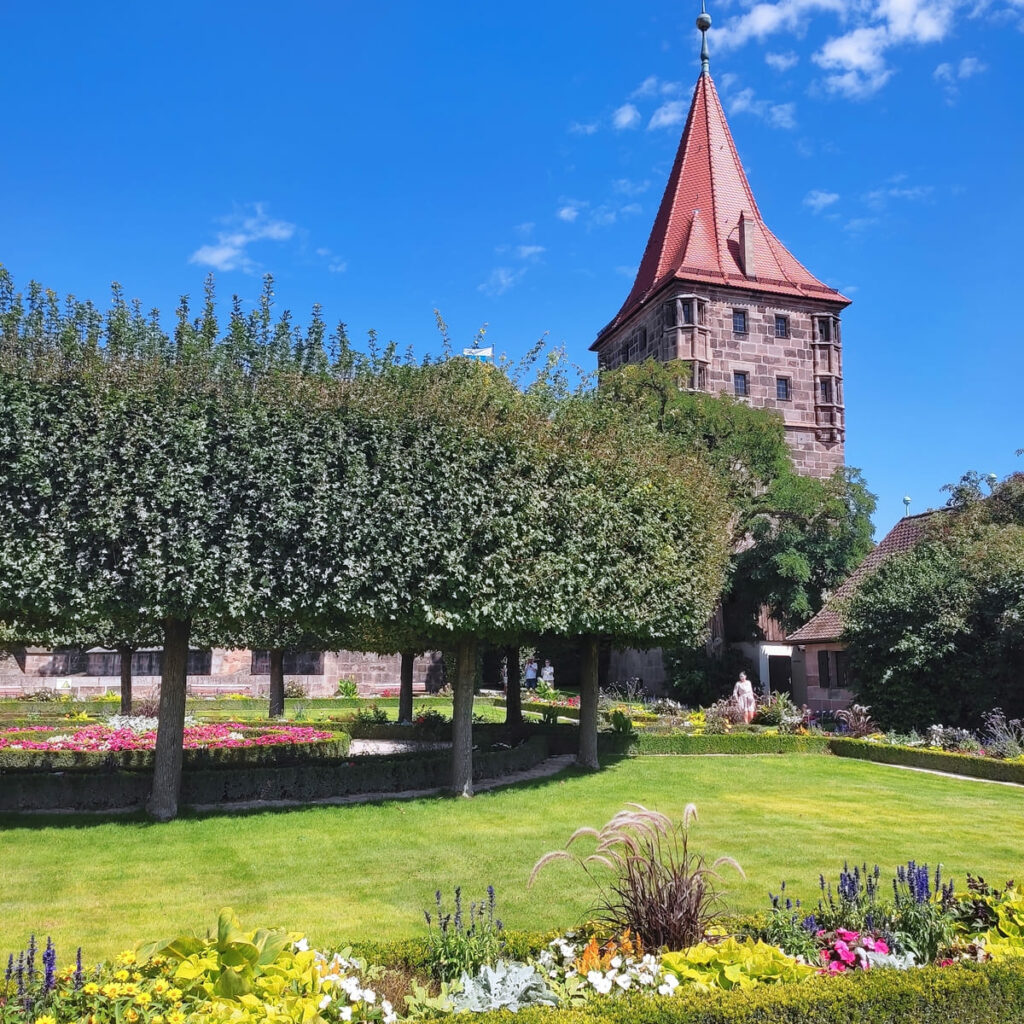 In Nuremberg's castle gardens manicured trees form a circle, surrounded by lawns and colorful flower borders.