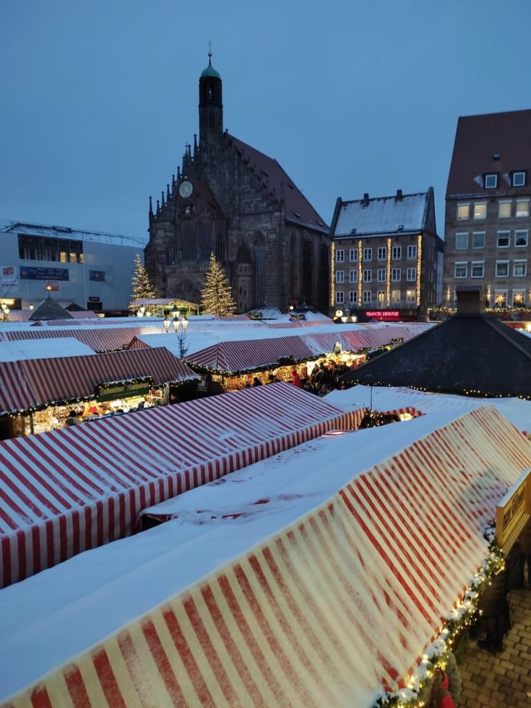 Christmas Market in Nuremberg in front of old church. There is a little bit of snow on the red-and-white striped roofs of the stalls